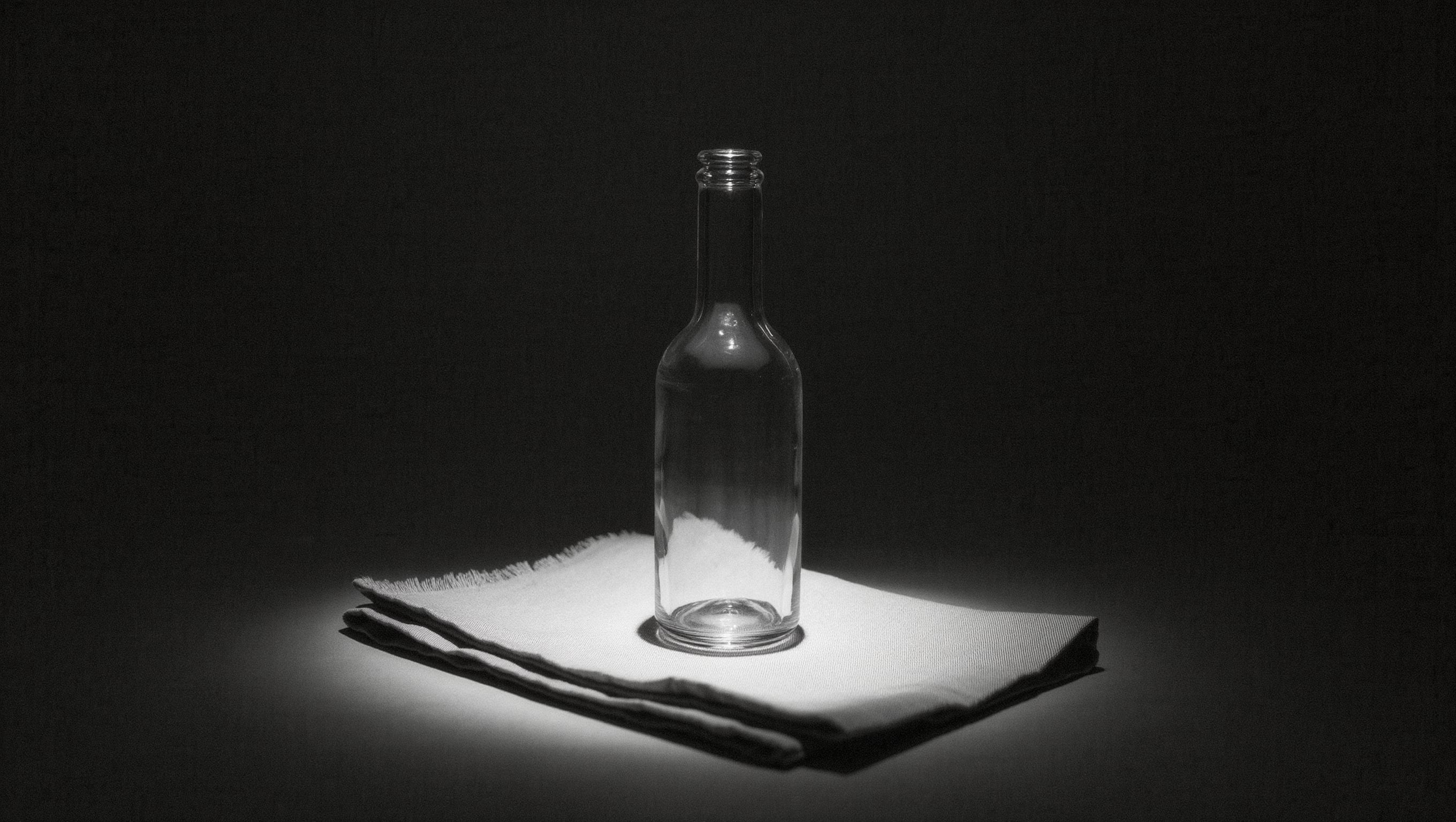 Ruhig gedeckter Behandlungsplatz mit gefaltetem Tuch und einer schmalen Glasflasche, gedämpftes Licht von oben